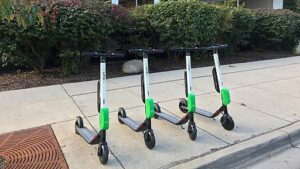 Four lime scooters parked on a sidwalk.