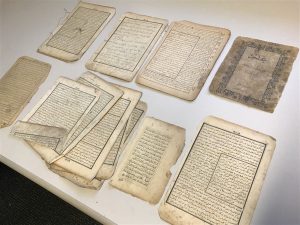 A selection of the damaged pages of books and manuscripts laid on a table. There are two rows and four columns of stacked pages.