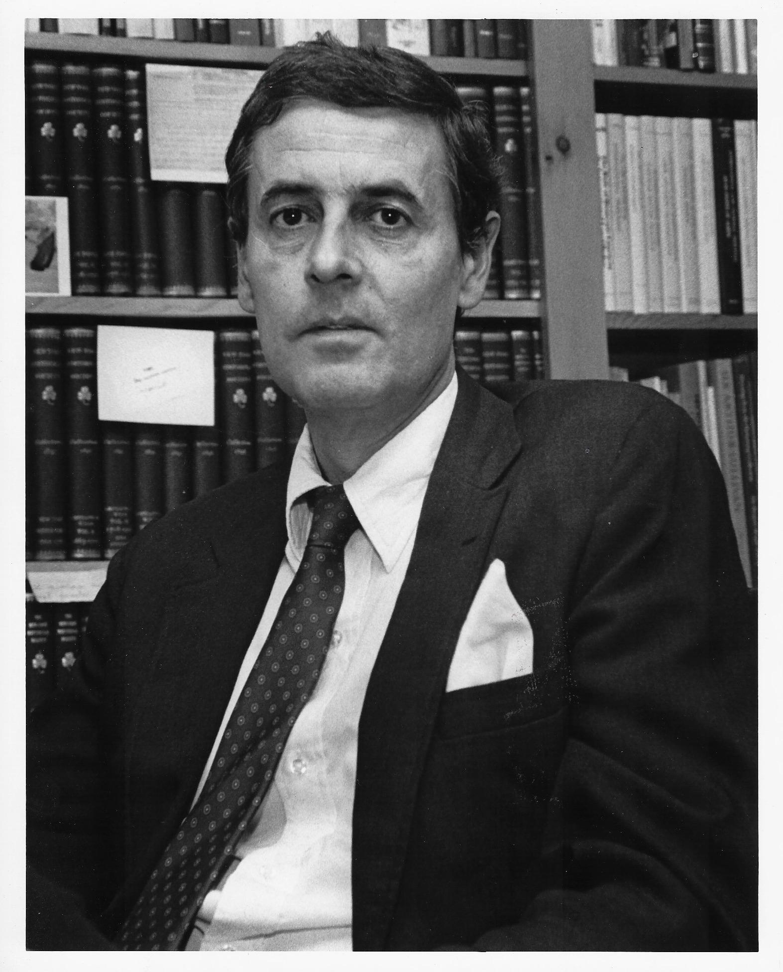 Black and white portrait of Wilson Walker Cowen in black suit and tie in front of bookshelves.